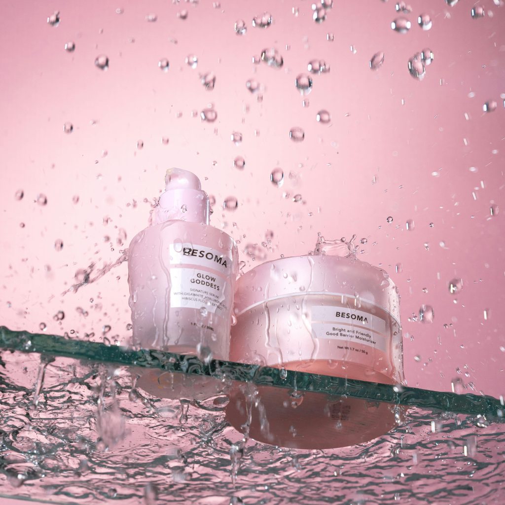 Dynamic display of skincare bottles on a glass shelf with cascading water in a pink setting.